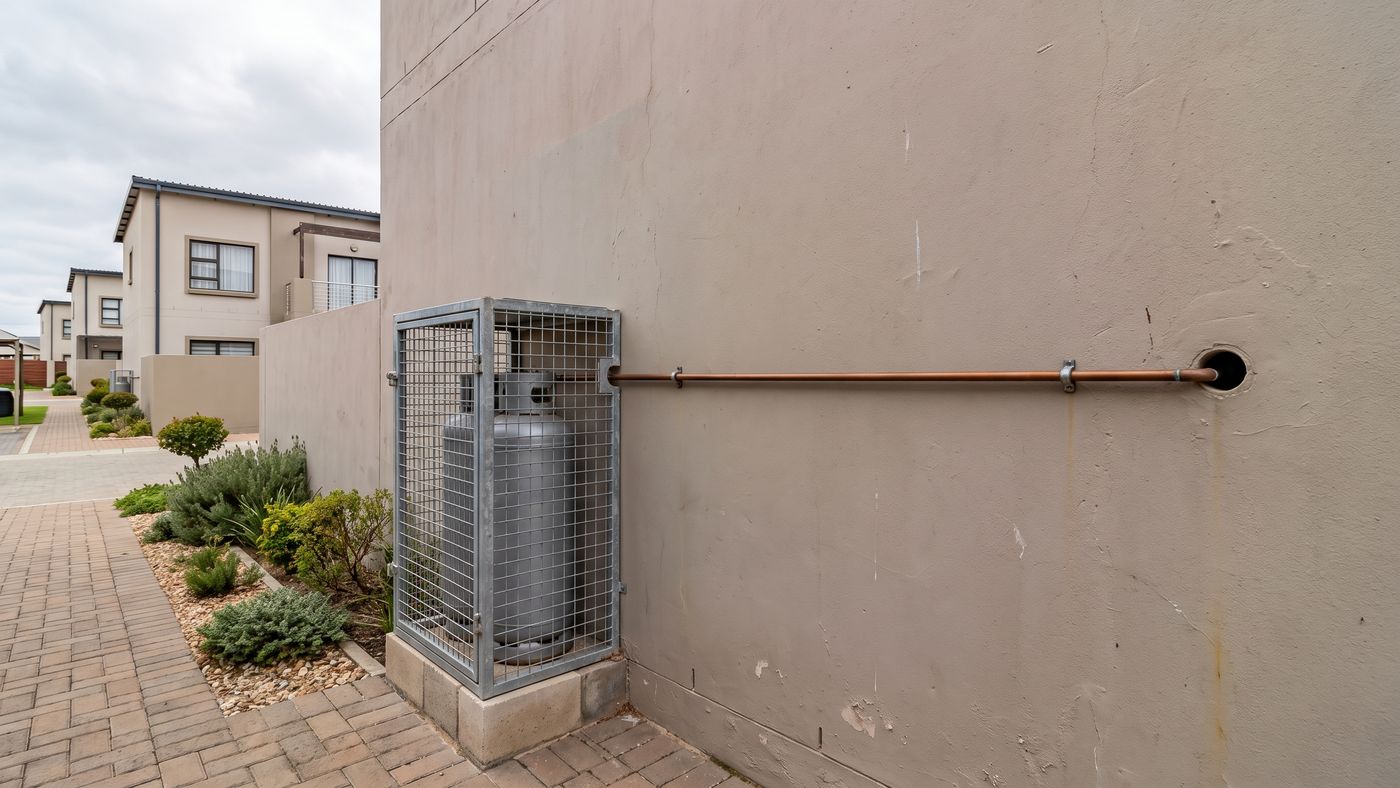 Caged gas cylinder against a blank side wall of a townhouse